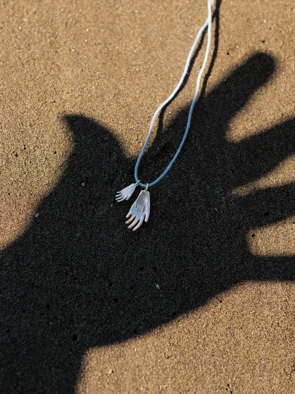 Pendant with the imprint of a child’s hand, cast in shadow on sand